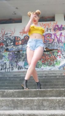 Dikey. Kız kizomba yapıyor. Grafiti arka planında dans eden seksi, komik kadın. Güzel genç dansçı baştan çıkarıcı bir şekilde dans eder ve kalçasını oynatır. Graffiti, kaykay parkı.