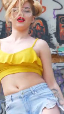 Dikey. Kız kizomba yapıyor. Grafiti arka planında dans eden seksi, komik kadın. Güzel genç dansçı baştan çıkarıcı bir şekilde dans eder ve kalçasını oynatır. Graffiti, kaykay parkı.