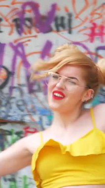 Dikey. Kız kizomba yapıyor. Grafiti arka planında dans eden seksi, komik kadın. Güzel genç dansçı baştan çıkarıcı bir şekilde dans eder ve kalçasını oynatır. Graffiti, kaykay parkı.