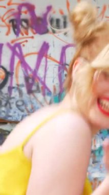 Dikey. Kız kizomba yapıyor. Grafiti arka planında dans eden seksi, komik kadın. Güzel genç dansçı baştan çıkarıcı bir şekilde dans eder ve kalçasını oynatır. Graffiti, kaykay parkı.