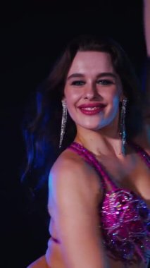 Dikey. Zarif giyimli bir kadın, müziğe gidiyor ve karanlık bir ortamda dans ediyor. Mor elbiseli kadın loş ışıklı odada zarif bir şekilde göbek dansı yapıyor. Gölgeli alanda mor elbiseler giyen kadın dansçı. Karanlıktaki kadın 