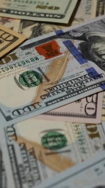 Dikey. Canlı bir Amerikan para akışı var. Çok renkli ışıkta yıkanmış bir Amerikan doları yağmuru. ABD banknotlarının yakın plan görüntüsü. Detayları renkli bir renge bürünmüş. kağıt para döner.