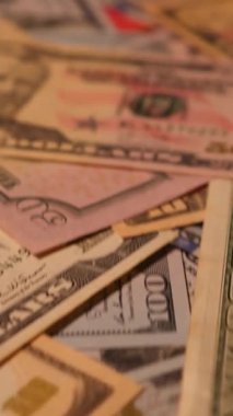 Dikey. Canlı bir Amerikan para akışı var. Çok renkli ışıkta yıkanmış bir Amerikan doları yağmuru. ABD banknotlarının yakın plan görüntüsü. Detayları renkli bir renge bürünmüş. kağıt para döner.