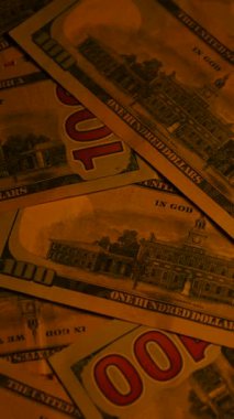 Dikey. Canlı bir Amerikan para akışı var. Çok renkli ışıkta yıkanmış bir Amerikan doları yağmuru. ABD banknotlarının yakın plan görüntüsü. Detayları renkli bir renge bürünmüş. kağıt para döner.