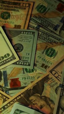 Dikey. Canlı bir Amerikan para akışı var. Çok renkli ışıkta yıkanmış bir Amerikan doları yağmuru. ABD banknotlarının yakın plan görüntüsü. Detayları renkli bir renge bürünmüş. kağıt para döner.