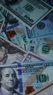 Dikey. Canlı bir Amerikan para akışı var. Çok renkli ışıkta yıkanmış bir Amerikan doları yağmuru. ABD banknotlarının yakın plan görüntüsü. Detayları renkli bir renge bürünmüş. kağıt para döner.