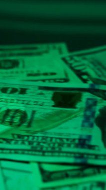 Dikey. Canlı bir Amerikan para akışı var. Çok renkli ışıkta yıkanmış bir Amerikan doları yağmuru. ABD banknotlarının yakın plan görüntüsü. Detayları renkli bir renge bürünmüş. kağıt para döner.