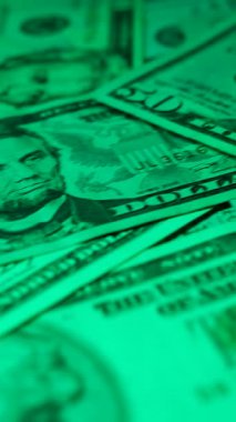 Dikey. Canlı bir Amerikan para akışı var. Çok renkli ışıkta yıkanmış bir Amerikan doları yağmuru. ABD banknotlarının yakın plan görüntüsü. Detayları renkli bir renge bürünmüş. kağıt para döner.