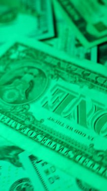 Dikey. Canlı bir Amerikan para akışı var. Çok renkli ışıkta yıkanmış bir Amerikan doları yağmuru. ABD banknotlarının yakın plan görüntüsü. Detayları renkli bir renge bürünmüş. kağıt para döner.