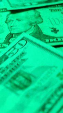 Dikey. Canlı bir Amerikan para akışı var. Çok renkli ışıkta yıkanmış bir Amerikan doları yağmuru. ABD banknotlarının yakın plan görüntüsü. Detayları renkli bir renge bürünmüş. kağıt para döner.