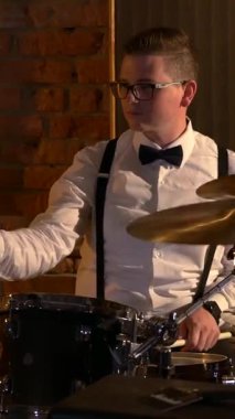 Dikey. Beyaz gömlekli adam stüdyoda davul çalıyor. Müzik grubu restoranda çalar. Gece romantik bir ışıktır. Jazz, Blues, Funk Retro stüdyosu, tuğla iç mekan.