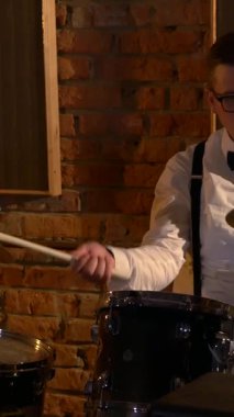 Dikey. Beyaz gömlekli adam stüdyoda davul çalıyor. Müzik grubu restoranda çalar. Gece romantik bir ışıktır. Jazz, Blues, Funk Retro stüdyosu, tuğla iç mekan.