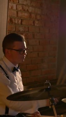 Dikey. Beyaz gömlekli adam stüdyoda davul çalıyor. Müzik grubu restoranda çalar. Gece romantik bir ışıktır. Jazz, Blues, Funk Retro stüdyosu, tuğla iç mekan.