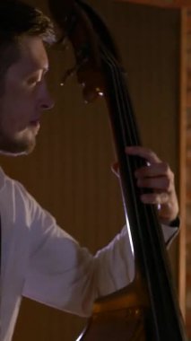 Dikey. Adam stüdyoda bas gitar çalıyor. İplerin ve pulların makro çekimi. Müzik grubu restoranda çalar. Gece romantik bir ışıktır. Caz, Blues, Funk Retro Stüdyosu,