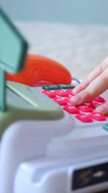 Dikey. Bir çocuğun elleri oyuncak kasasının renkli tuşlarına basıyor. Minyatür bir kasadaki düğmelere titizlikle basan bir çocuğun parmak görüntüsü. Çocuk yazar kasası.