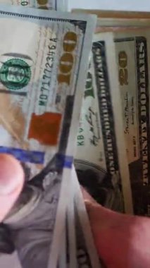 Dikey. Bir yığın gevrek, dolar banknotları, becerikli ellerde tutuluyor. Adam kağıt para sayıyor. Bir Amerikan para akışı. Bir sürü dolar. ABD banknotlarının yakın plan görüntüsü. İşadamı banknotları sayar