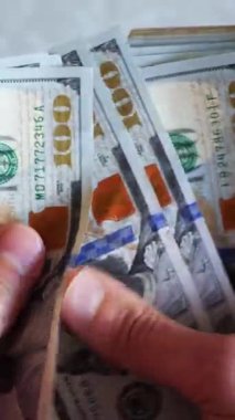 Dikey. Bir yığın gevrek, dolar banknotları, becerikli ellerde tutuluyor. Adam kağıt para sayıyor. Bir Amerikan para akışı. Bir sürü dolar. ABD banknotlarının yakın plan görüntüsü. İşadamı banknotları sayar
