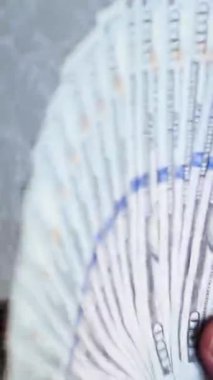 Dikey. Bir yığın gevrek, dolar banknotları, becerikli ellerde tutuluyor. Adam kağıt para sayıyor. Bir Amerikan para akışı. Bir sürü dolar. ABD banknotlarının yakın plan görüntüsü. İşadamı banknotları sayar