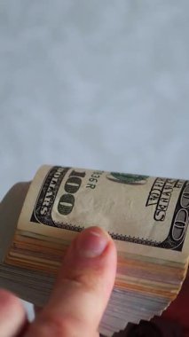 Dikey. Bir yığın gevrek, dolar banknotları, becerikli ellerde tutuluyor. Adam kağıt para sayıyor. Bir Amerikan para akışı. Bir sürü dolar. ABD banknotlarının yakın plan görüntüsü. İşadamı banknotları sayar