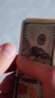 Dikey. Bir yığın gevrek, dolar banknotları, becerikli ellerde tutuluyor. Adam kağıt para sayıyor. Bir Amerikan para akışı. Bir sürü dolar. ABD banknotlarının yakın plan görüntüsü. İşadamı banknotları sayar