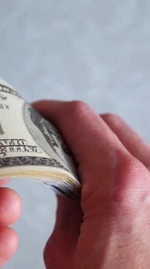Dikey. Bir yığın gevrek, dolar banknotları, becerikli ellerde tutuluyor. Adam kağıt para sayıyor. Bir Amerikan para akışı. Bir sürü dolar. ABD banknotlarının yakın plan görüntüsü. İşadamı banknotları sayar