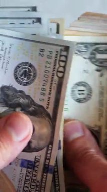 Dikey. Bir yığın gevrek, dolar banknotları, becerikli ellerde tutuluyor. Adam kağıt para sayıyor. Bir Amerikan para akışı. Bir sürü dolar. ABD banknotlarının yakın plan görüntüsü. İşadamı banknotları sayar