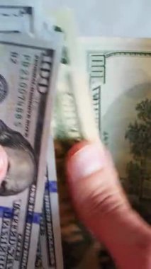 Dikey. Bir yığın gevrek, dolar banknotları, becerikli ellerde tutuluyor. Adam kağıt para sayıyor. Bir Amerikan para akışı. Bir sürü dolar. ABD banknotlarının yakın plan görüntüsü. İşadamı banknotları sayar