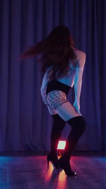 Dikey. Külotlu, tişörtlü, siyah çizmeli, baştan çıkarıcı dans eden seksi bir kadın. Bir dansçı kız karanlık bir salonda erotik bir şekilde dans eder. Kıvırma, striptiz. Atmosferik renkli ışık, kulüp, sahne.