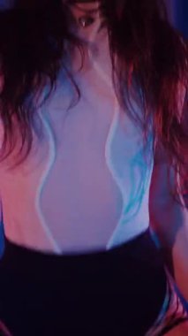 Dikey. Külotlu, tişörtlü, siyah çizmeli, baştan çıkarıcı dans eden seksi bir kadın. Bir dansçı kız karanlık bir salonda erotik bir şekilde dans eder. Kıvırma, striptiz. Atmosferik renkli ışık, kulüp, sahne.