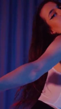 Dikey. Külotlu, tişörtlü, siyah çizmeli, baştan çıkarıcı dans eden seksi bir kadın. Bir dansçı kız karanlık bir salonda erotik bir şekilde dans eder. Kıvırma, striptiz. Atmosferik renkli ışık, kulüp, sahne.