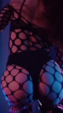 Dikey. Dans eden örgü giysili seksi kadın. Bir dansçı kız karanlık bir salonda erotik bir şekilde dans eder. Kıvranma, yüksek topuklar, striptiz, baştan çıkarıcı bir dans. Atmosferik renkli ışık, kulüp, sahne.
