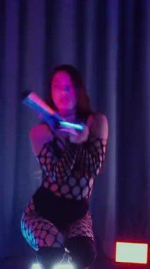 Dikey. Dans eden örgü giysili seksi kadın. Bir dansçı kız karanlık bir salonda erotik bir şekilde dans eder. Kıvranma, yüksek topuklar, striptiz, baştan çıkarıcı bir dans. Atmosferik renkli ışık, kulüp, sahne.