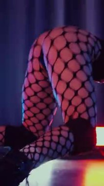Dikey. Dans eden örgü giysili seksi kadın. Bir dansçı kız karanlık bir salonda erotik bir şekilde dans eder. Kıvranma, yüksek topuklar, striptiz, baştan çıkarıcı bir dans. Atmosferik renkli ışık, kulüp, sahne.