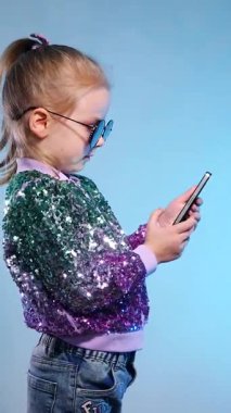 Dikey. Pullu ceketiyle göz kamaştıran küçük bir kız, cep telefonuna sarılmış, ifadesi neşe dolu bir sürpriz. Genç, neşeli bir kız telefonda konuşur ve güler. Cep telefonu olan mutlu bir çocuk. Selfie