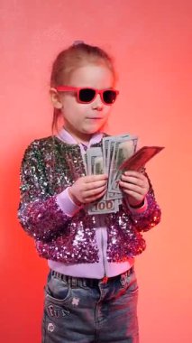 Dikey. Pullu ceketiyle göz kamaştıran genç bir kız, yığınla para, dolar banknotlarının hayranı. Küçük bir girişimci bir yığın parayla para sayar. Kazan, piyango. Para hareket halinde. Para dans eder