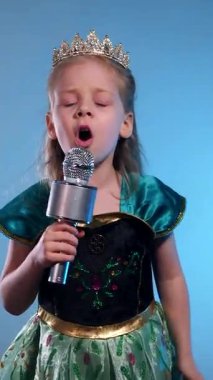 Dikey. Küçük bir prenses, yükselen bir ses, büyüleyici bir performans. Kraliçe mikrofona şarkı söyleyip dans ediyor. Karaoke. Zümrüt bir elbise, parlak bir taç, küçük bir yıldız adayı sahneye çıkıyor. Eller birbirine kenetlendi