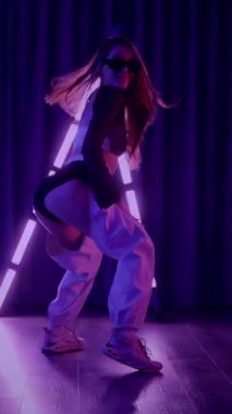 Dikey. Baştan çıkarıcı dans eden seksi kadın. Titreyen bir dansçı, canlı mor ve mavi ışıkla yıkanmış, canlı neon bir üçgenin altında sahnenin enerjisini somutlaştırıyor. Bir sanatçının kadın vücudu.