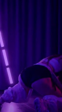 Dikey. Baştan çıkarıcı dans eden seksi kadın. Titreyen bir dansçı, canlı mor ve mavi ışıkla yıkanmış, canlı neon bir üçgenin altında sahnenin enerjisini somutlaştırıyor. Bir sanatçının kadın vücudu.