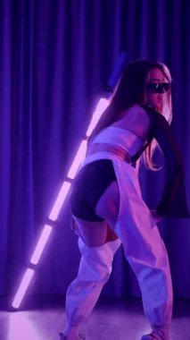 Dikey. Baştan çıkarıcı dans eden seksi kadın. Titreyen bir dansçı, canlı mor ve mavi ışıkla yıkanmış, canlı neon bir üçgenin altında sahnenin enerjisini somutlaştırıyor. Bir sanatçının kadın vücudu.