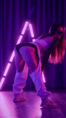 Dikey. Baştan çıkarıcı dans eden seksi kadın. Titreyen bir dansçı, canlı mor ve mavi ışıkla yıkanmış, canlı neon bir üçgenin altında sahnenin enerjisini somutlaştırıyor. Bir sanatçının kadın vücudu.