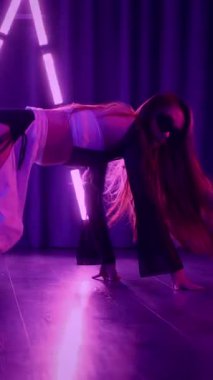 Dikey. Baştan çıkarıcı dans eden seksi kadın. Titreyen bir dansçı, canlı mor ve mavi ışıkla yıkanmış, canlı neon bir üçgenin altında sahnenin enerjisini somutlaştırıyor. Bir sanatçının kadın vücudu.