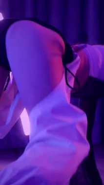 Dikey. Baştan çıkarıcı dans eden seksi kadın. Titreyen bir dansçı, canlı mor ve mavi ışıkla yıkanmış, canlı neon bir üçgenin altında sahnenin enerjisini somutlaştırıyor. Bir sanatçının kadın vücudu.