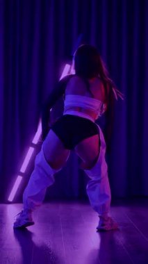 Dikey. Baştan çıkarıcı dans eden seksi kadın. Titreyen bir dansçı, canlı mor ve mavi ışıkla yıkanmış, canlı neon bir üçgenin altında sahnenin enerjisini somutlaştırıyor. Bir sanatçının kadın vücudu.