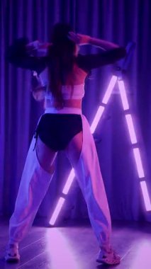 Dikey. Baştan çıkarıcı dans eden seksi kadın. Titreyen bir dansçı, canlı mor ve mavi ışıkla yıkanmış, canlı neon bir üçgenin altında sahnenin enerjisini somutlaştırıyor. Bir sanatçının kadın vücudu.