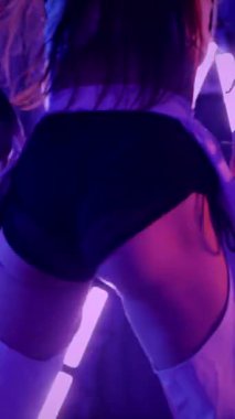 Dikey. Baştan çıkarıcı dans eden seksi kadın. Titreyen bir dansçı, canlı mor ve mavi ışıkla yıkanmış, canlı neon bir üçgenin altında sahnenin enerjisini somutlaştırıyor. Bir sanatçının kadın vücudu.