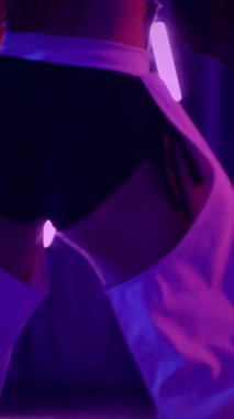 Dikey. Baştan çıkarıcı dans eden seksi kadın. Titreyen bir dansçı, canlı mor ve mavi ışıkla yıkanmış, canlı neon bir üçgenin altında sahnenin enerjisini somutlaştırıyor. Bir sanatçının kadın vücudu.