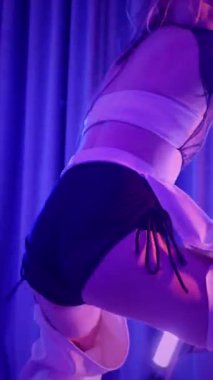 Dikey. Baştan çıkarıcı dans eden seksi kadın. Titreyen bir dansçı, canlı mor ve mavi ışıkla yıkanmış, canlı neon bir üçgenin altında sahnenin enerjisini somutlaştırıyor. Bir sanatçının kadın vücudu.