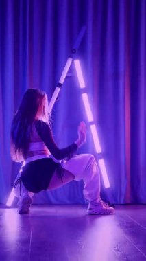 Dikey. Baştan çıkarıcı dans eden seksi kadın. Titreyen bir dansçı, canlı mor ve mavi ışıkla yıkanmış, canlı neon bir üçgenin altında sahnenin enerjisini somutlaştırıyor. Bir sanatçının kadın vücudu.