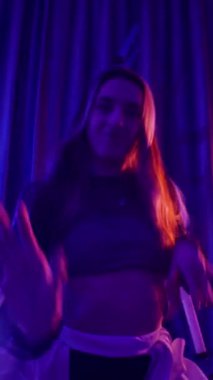 Dikey. Baştan çıkarıcı dans eden seksi kadın. Titreyen bir dansçı, canlı mor ve mavi ışıkla yıkanmış, canlı neon bir üçgenin altında sahnenin enerjisini somutlaştırıyor. Bir sanatçının kadın vücudu.