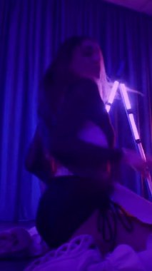 Dikey. Baştan çıkarıcı dans eden seksi kadın. Titreyen bir dansçı, canlı mor ve mavi ışıkla yıkanmış, canlı neon bir üçgenin altında sahnenin enerjisini somutlaştırıyor. Bir sanatçının kadın vücudu.